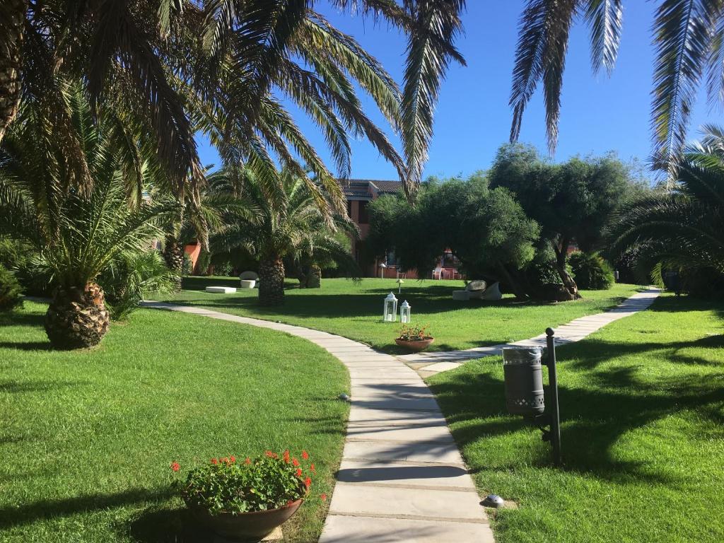 a walking path through a park with palm trees at Cala Rosa Club Hotel in Stintino