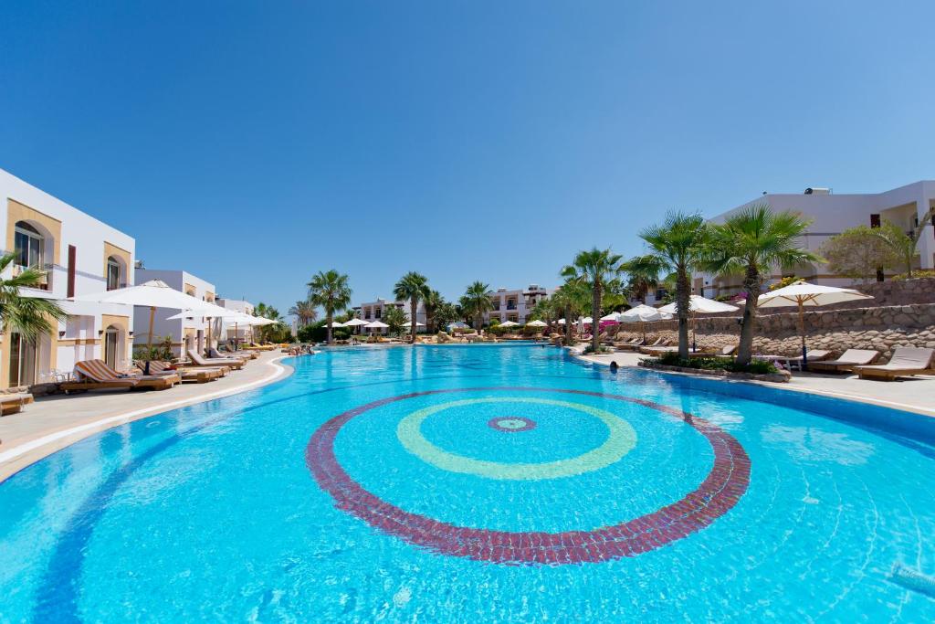 une grande piscine avec des chaises et des parasols dans un complexe dans l'établissement Amphoras Blu, à Charm el-Cheikh