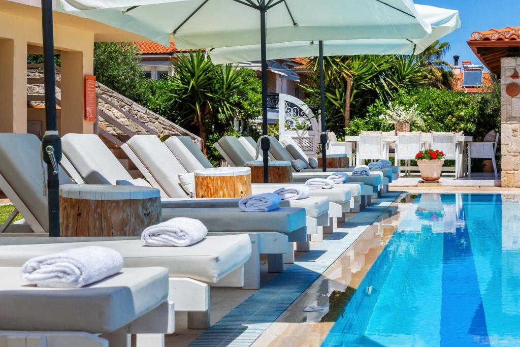 a row of chaise lounge chairs next to a swimming pool at Hesperides Hotel Pefkochori in Pefkochori
