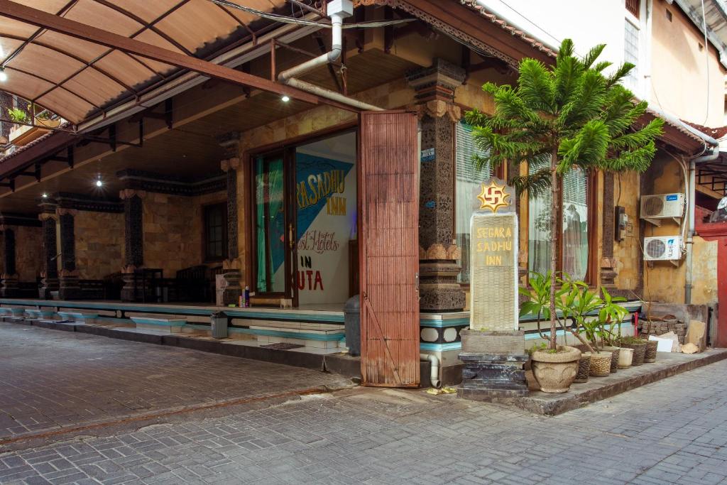 a building with a palm tree in front of it at Segara Sadhu Inn Kuta by ecommerceloka in Kuta