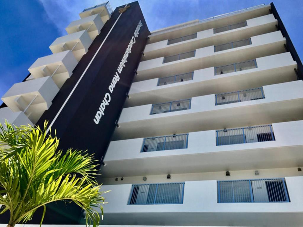 a tall white building with a palm tree in front of it at Seaside Condominium Rana Chatan in Chatan