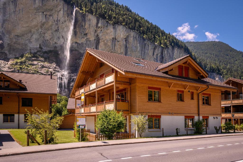 une grande maison en bois avec une cascade en arrière-plan dans l'établissement Apartment Breithorn - Charming home - free parking & Wifi, à Lauterbrunnen