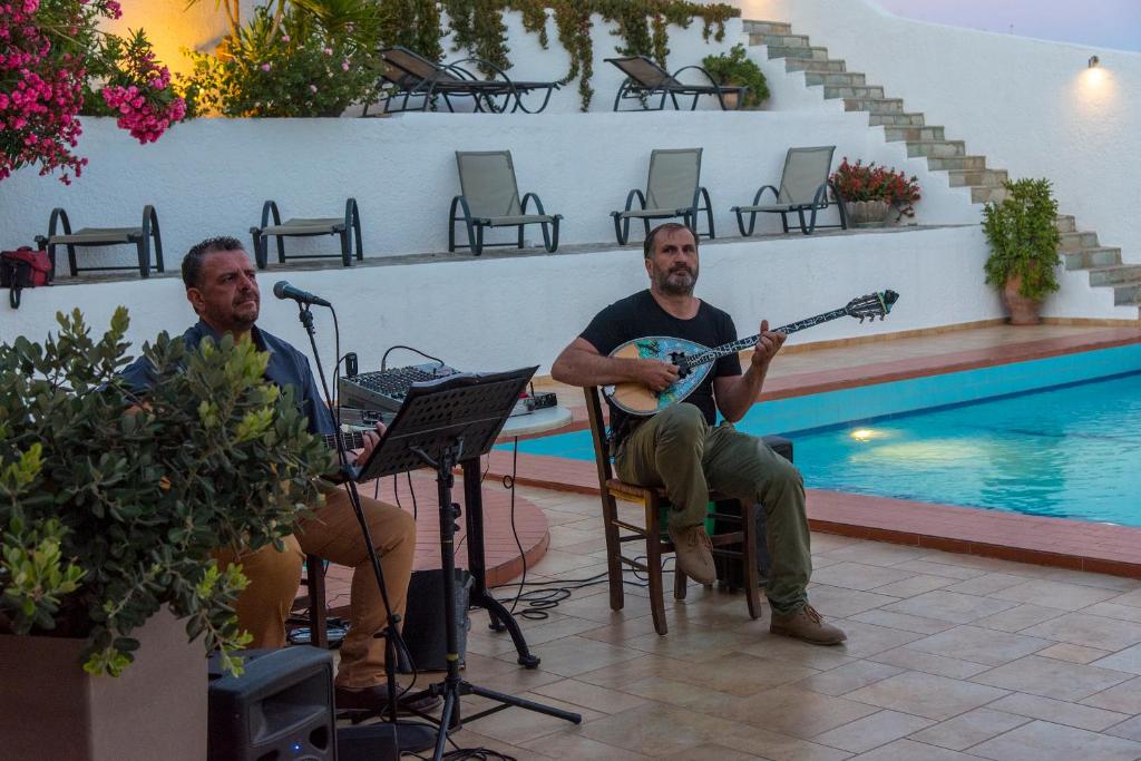 two men sitting in chairs playing guitar next to a pool at Castri Village Hotel in Palekastron
