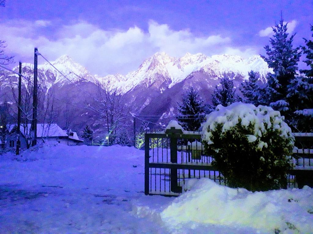 a snowy field with a fence and snow covered mountains at Casa Vacanza Pineta in Malonno