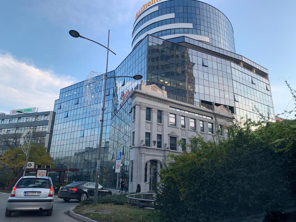 a building and a glass building with cars in front of it at Pupin Palace Apartments in Novi Sad