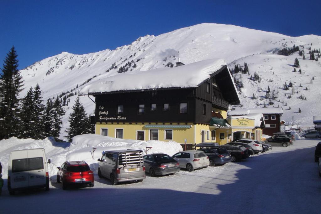 um edifício com carros estacionados num parque de estacionamento com uma montanha coberta de neve em Hotel Sportpension Reiter em Planneralm