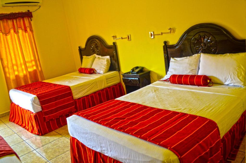 Hotel Plaza Palmero في سان بيدرو سولا: غرفة نوم بسريرين بملاءات حمراء وبيضاء