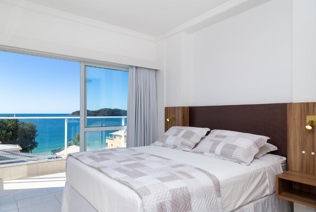 a white bedroom with a bed and a large window at Pousada Riviera Bombinhas in Bombinhas