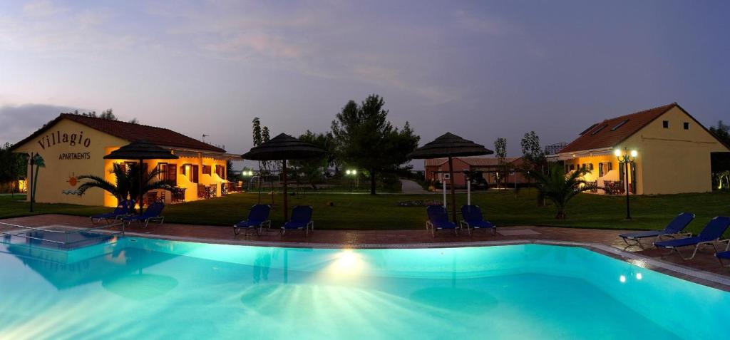 una piscina por la noche con sillas y sombrillas en Villagio, en Lefkada