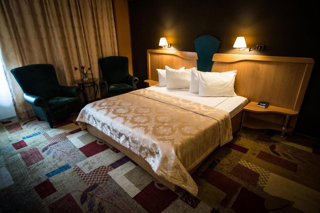 ein Hotelzimmer mit einem Bett und zwei Stühlen in der Unterkunft Ambassador Hotel in Timişoara