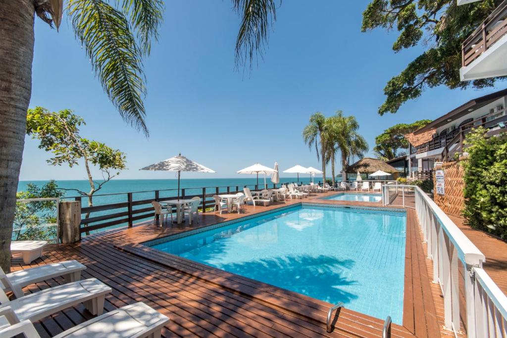 a swimming pool with chairs and the ocean in the background at Bombinhas Tourist Apart in Bombinhas