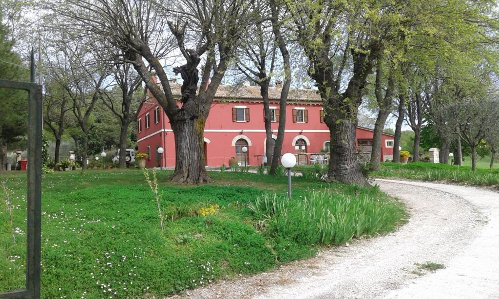 a red house with trees next to a dirt road at Casa Vacanze La Meridiana in Serrungarina