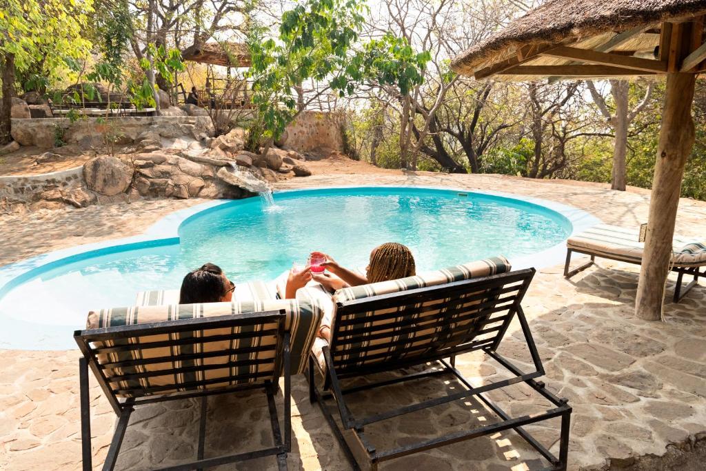 two people sitting in chairs in front of a swimming pool at Safari Beach Lodge in Senga