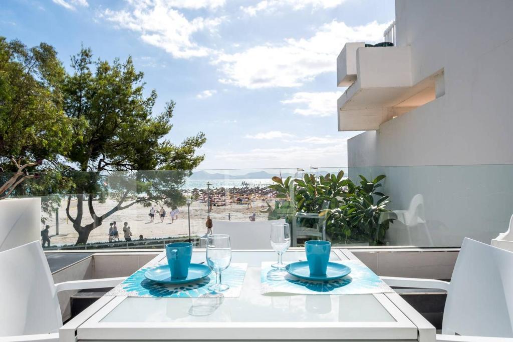 a white table with glasses on a balcony with a view of the beach at Ciudad Blanca Apartment in Port d'Alcudia