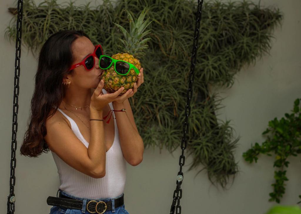 a woman with sunglasses eating a pineapple on a swing at La Vaina Cali in Cali
