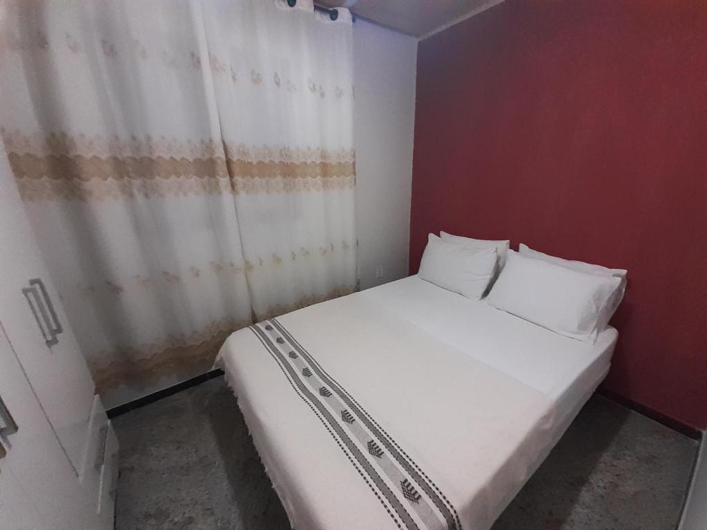 Cama blanca en habitación pequeña con cortina en residencia bem viver, en Arraial do Cabo