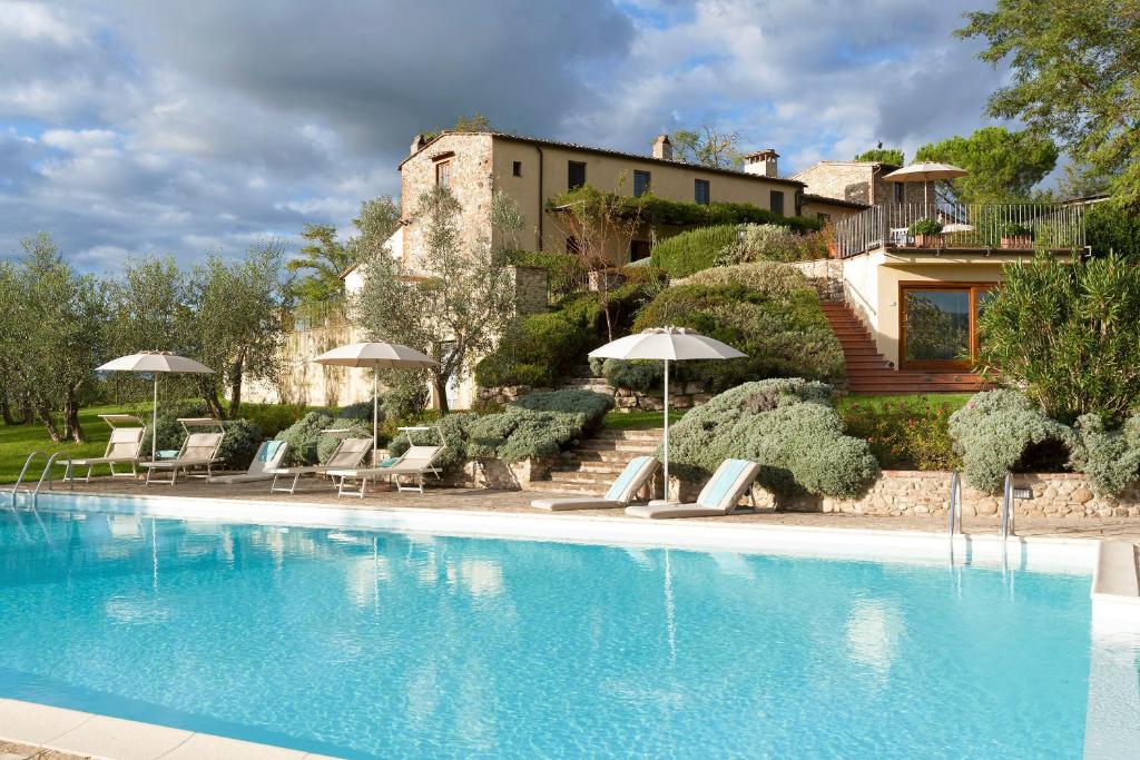 una piscina con sedie e ombrelloni di fronte a un edificio di Relais Poggio Borgoni a San Casciano in Val di Pesa