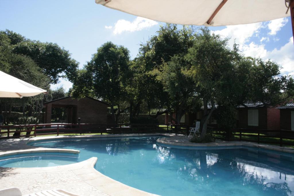 a large swimming pool with an umbrella and trees at Complejo Arco Iris in Villa Cura Brochero