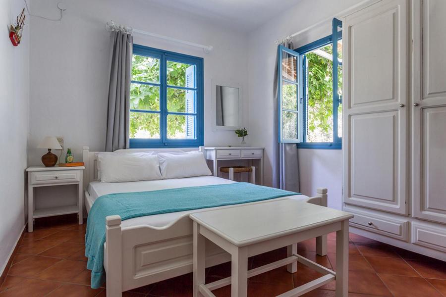 a white bedroom with a bed and two windows at Limnonari Studio in Skopelos Town