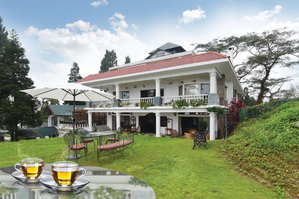 a large white house with a table with glasses on it at Sourenee Tea Estate in Mirik