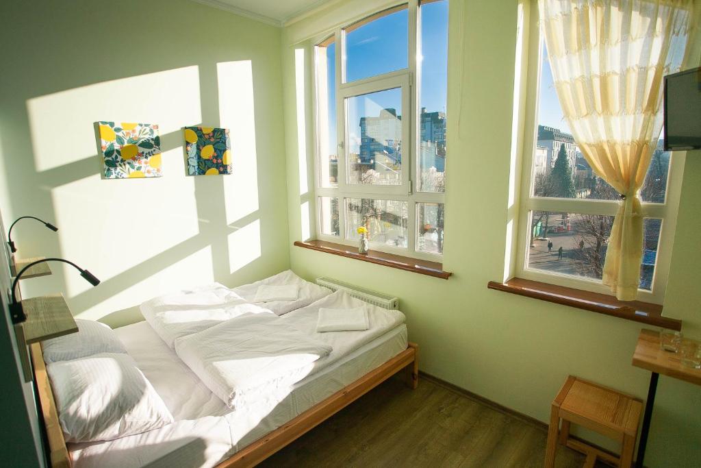 a bed in a room with two windows at DREAM Hostel Khmelnytskyi in Khmelʼnytsʼkyy