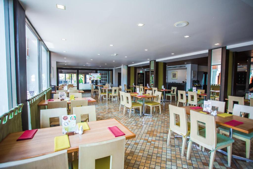 um restaurante com mesas e cadeiras de madeira e janelas em Phuket Merlin Hotel em Cidade Phuket