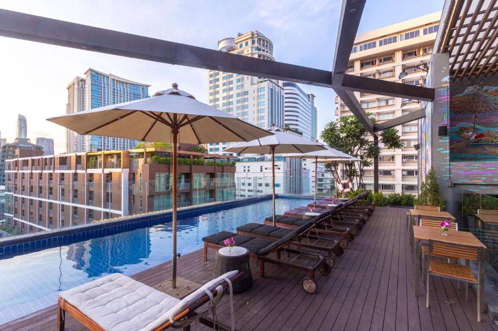 Hotel Icon Bangkok Sukhumvit 2 في بانكوك: مسبح على السطح مع طاولات ومظلات على مبنى