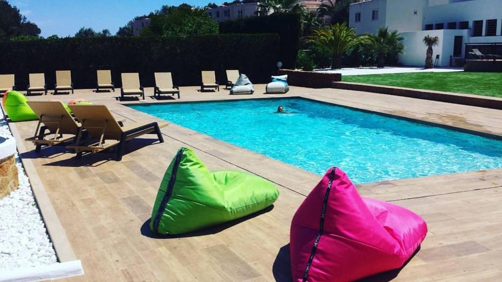 una piscina con sillas verdes y rosas junto a ella en Apartamentos Colomar, en Playa Es Figueral
