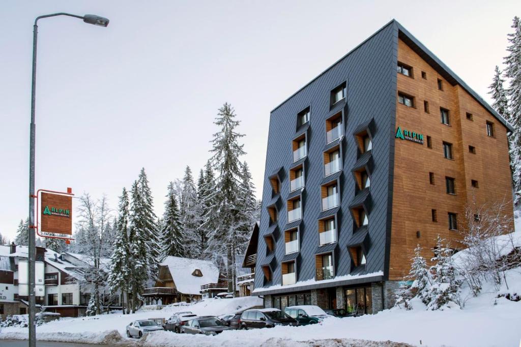 un edificio nella neve con macchine parcheggiate di fronte di Alpin Apartments Jahorina a Jahorina