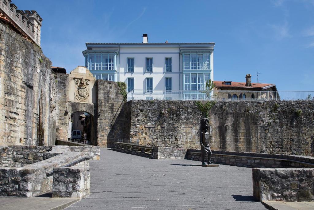 a building behind a stone wall with a statue at Hondarribia Suites in Hondarribia