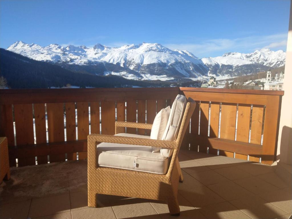 a wicker chair sitting on a balcony with snow covered mountains at Chesa Delfin in Pontresina