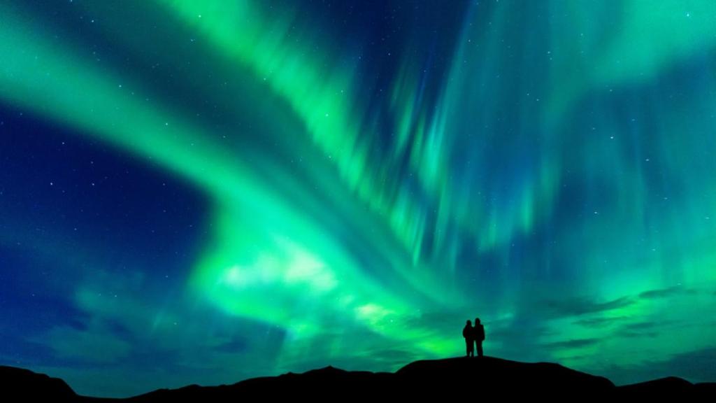 two people standing on top of a hill watching the northern lights at Yellow Dog Lodge, Inc. in Yellowknife