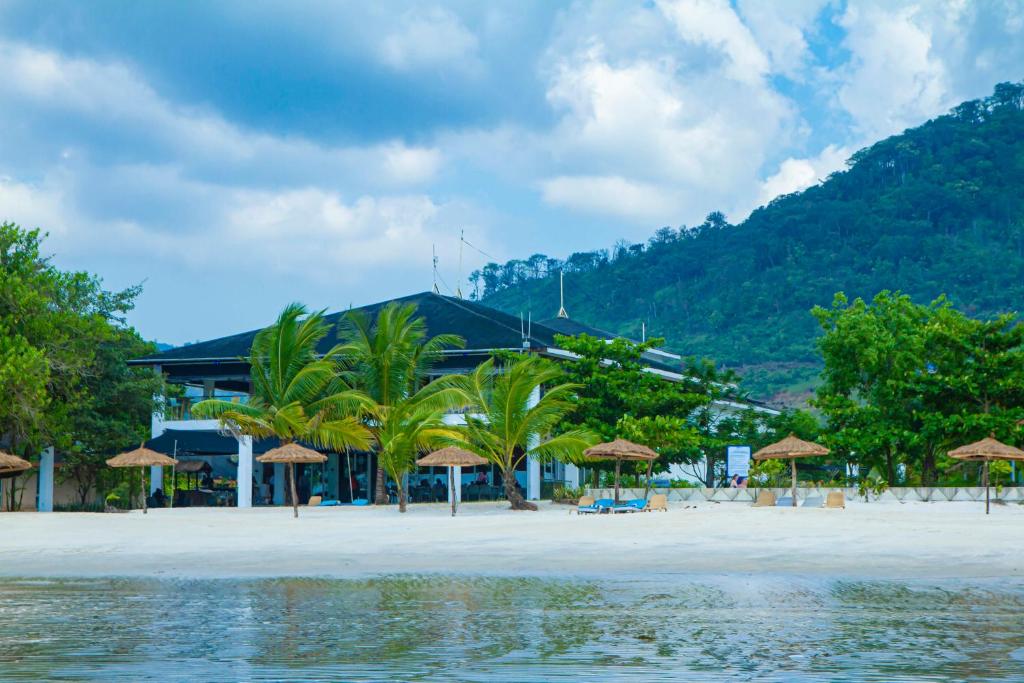 a beach with trees and umbrellas and a building at The Place Resort in Toke