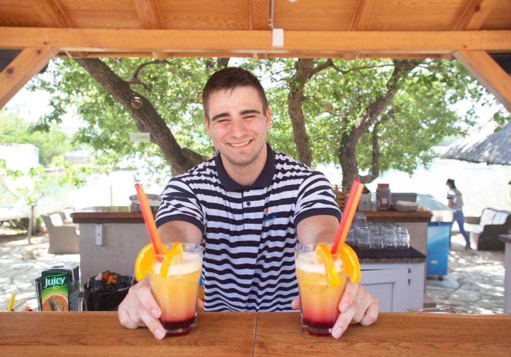 a man sitting at a table with two drinks at Krk Mobile Homes in Klimno