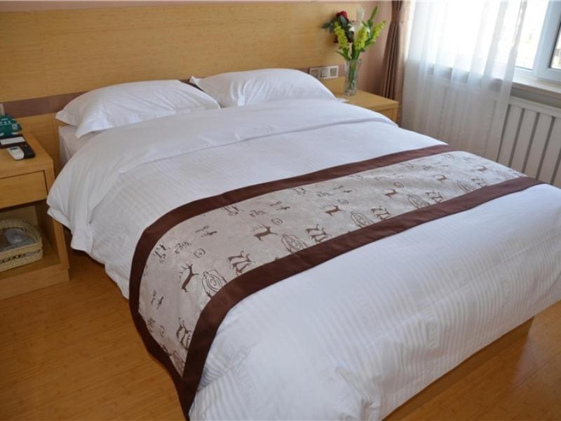 um quarto com uma cama com lençóis brancos e um vaso de flores em GreenTree Inn Shenyang Shengjing Hospital Shenyang Liaol Road Business Hotel em Shenyang