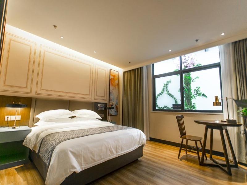 a bedroom with a bed and a table and a window at GME Bozhou Qiaocheng District Jian'an Road Railway Station Hotel in Bozhou