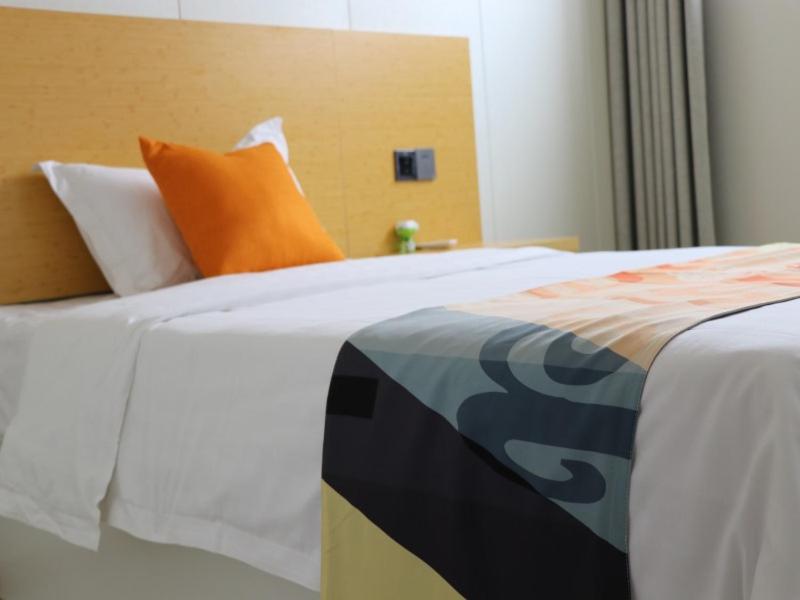 un letto con lenzuola bianche e un cuscino arancione di Shell Suzhou Chinese Medicine Hospital Hotel a Suzhou