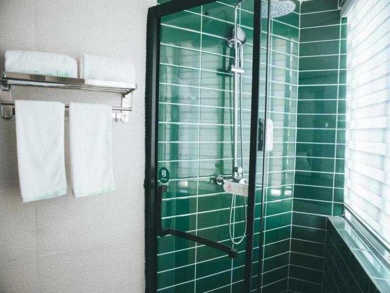 a green tiled shower in a bathroom with towels at GreenTree Inn Suzhou Railway Station Park Road Hotel in Suzhou