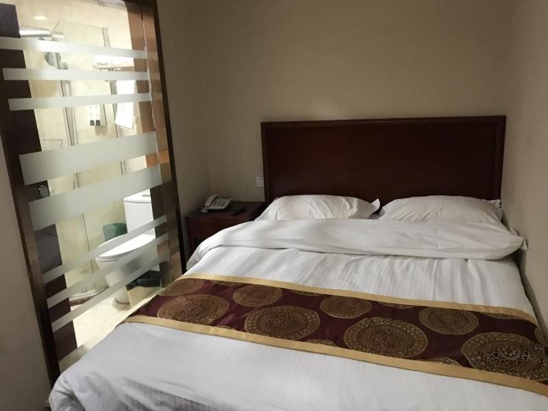 a bedroom with a large bed with a wooden headboard at GreenTree Inn Nantong Liuqiao Town Government Tongliu Road Express Hotel in Nantong