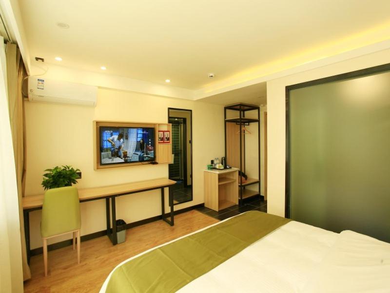 a bedroom with a bed and a desk with a television at GreenTree Inn Anlong County Zhaodi Hotel in Xingyi