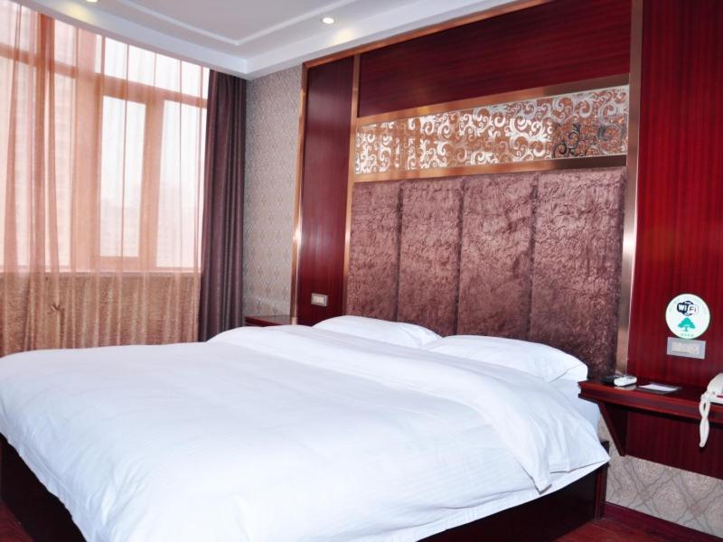 a bedroom with a large white bed with a wooden headboard at GreenTree Inn Lanzhou Railway Station East Road Business Hotel in Lanzhou