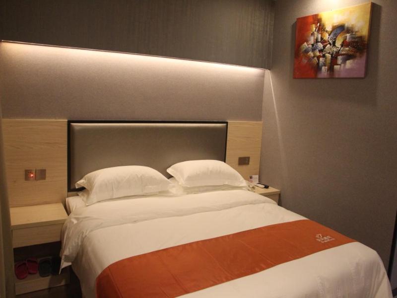 ein Schlafzimmer mit einem großen weißen Bett mit einem Gemälde an der Wand in der Unterkunft Shell Shanghai Chedun Yingshi City Yingshi Road Hotel in Shanghai