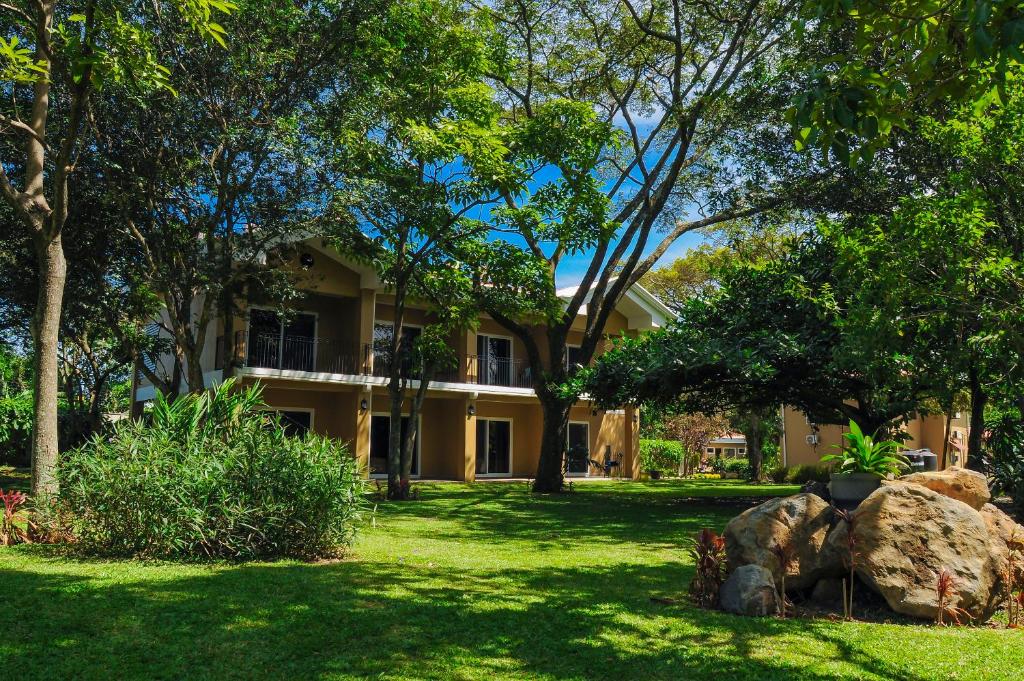 ein gelbes Haus mit einem Hof mit Bäumen und einem Felsen in der Unterkunft Hotel Robledal in Alajuela