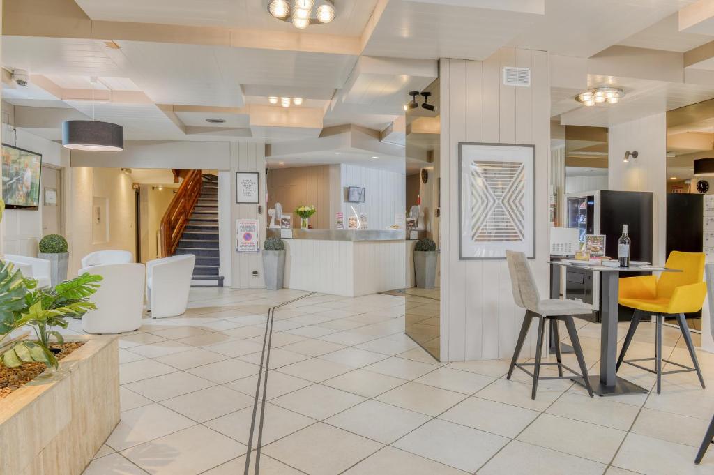 un vestíbulo con muebles blancos y sillas amarillas en Hotel Le Gambetta, en Bergerac