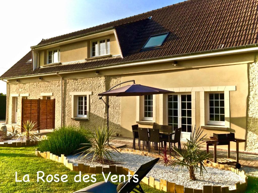 een huis met een tafel en een paraplu in de tuin bij La Rose Des Vents in Grandcamp-Maisy