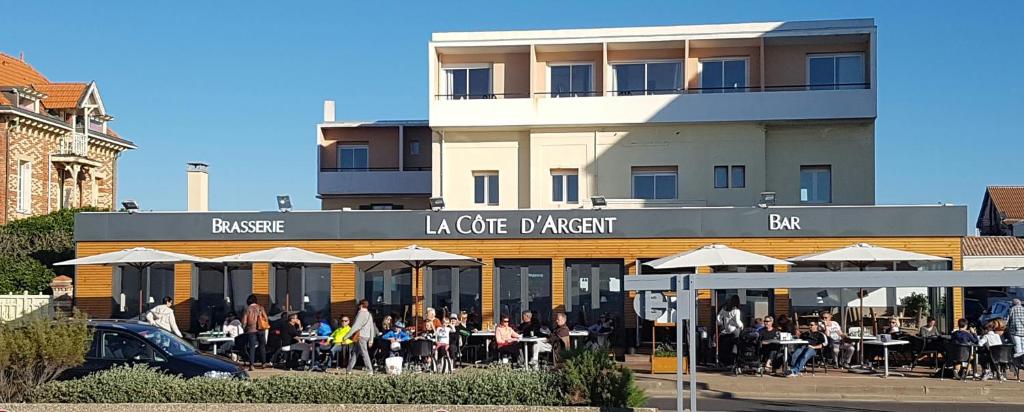 um grupo de pessoas sentadas em mesas fora de um edifício em Hotel Cote d'Argent em Lacanau-Océan