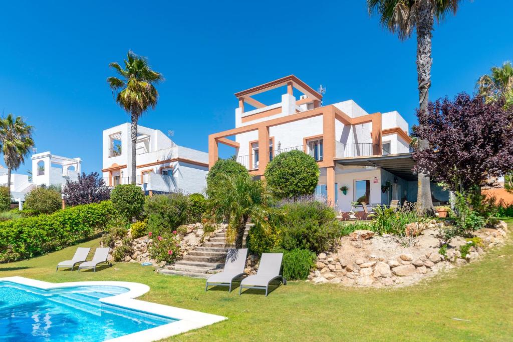 une grande maison avec une piscine et des palmiers dans l'établissement Villa Golf Sanlucar, à Sanlúcar de Barrameda