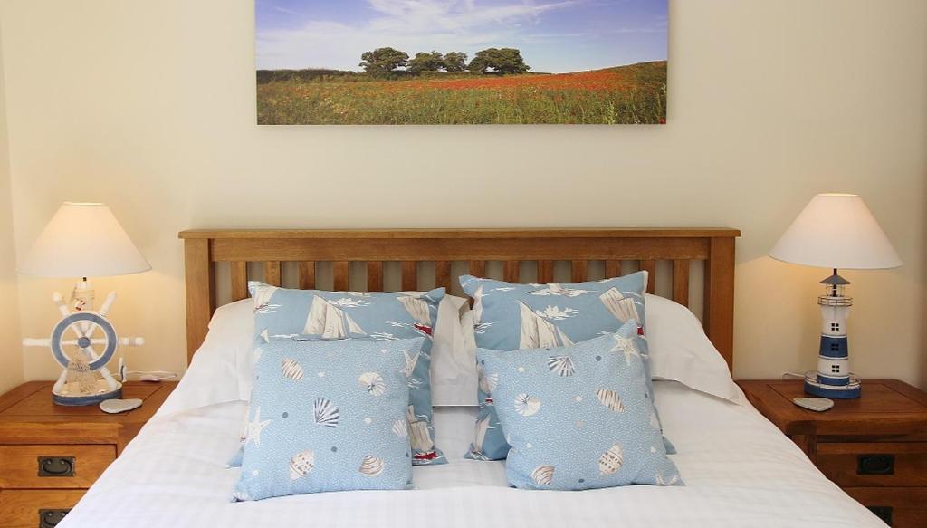 a bed with blue and white pillows and a painting at Heron's Hideaway in Wells next the Sea
