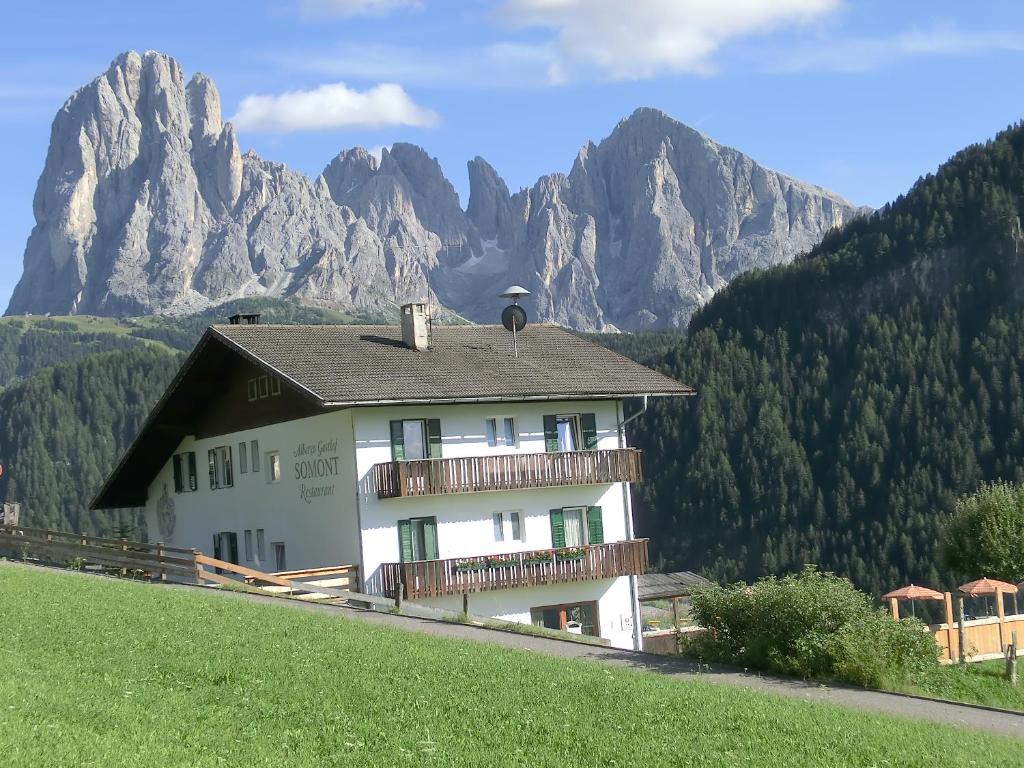 un bâtiment sur une colline avec des montagnes en arrière-plan dans l'établissement Albergo Somont, à Ortisei