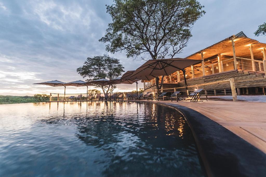 a pool of water with umbrellas in front of a building at Mdluli Safari Lodge in Hazyview